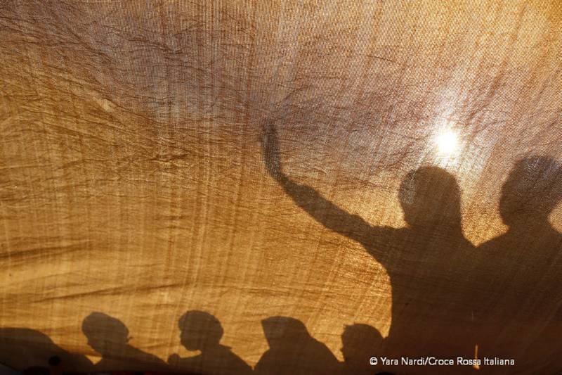 Le silhouette dei migranti si intravedono dietro un telo. Foto: Yara Nardi - Croce Rossa