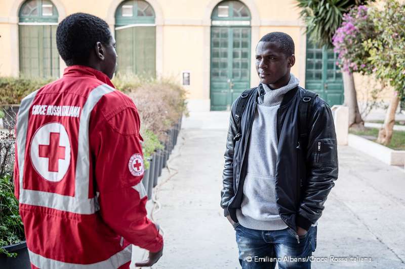 Un volontario di Croce Rossa Italiana parla con un ragazzo migrante