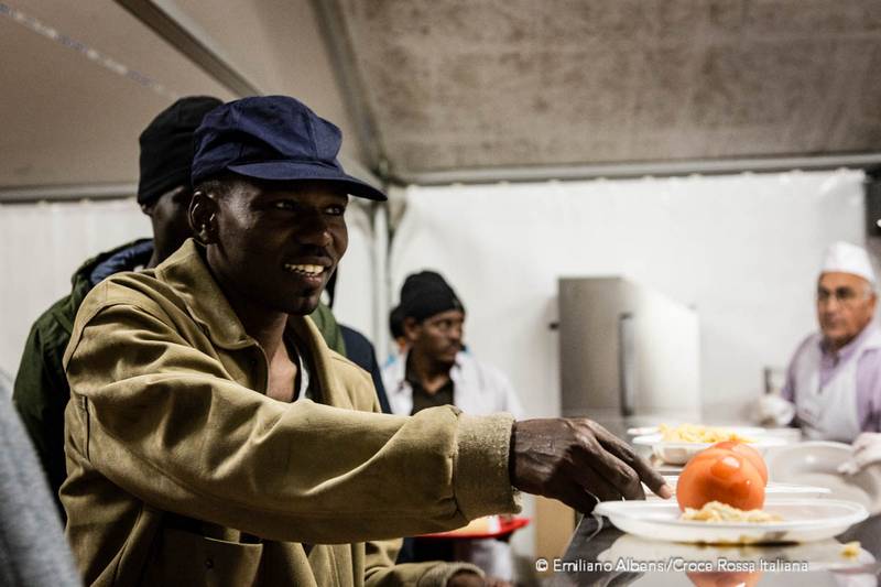 Campo Roya di Ventimiglia, la fila per la mensa della Croce Rossa: un uomo prende il piatto pronto con un sorriso