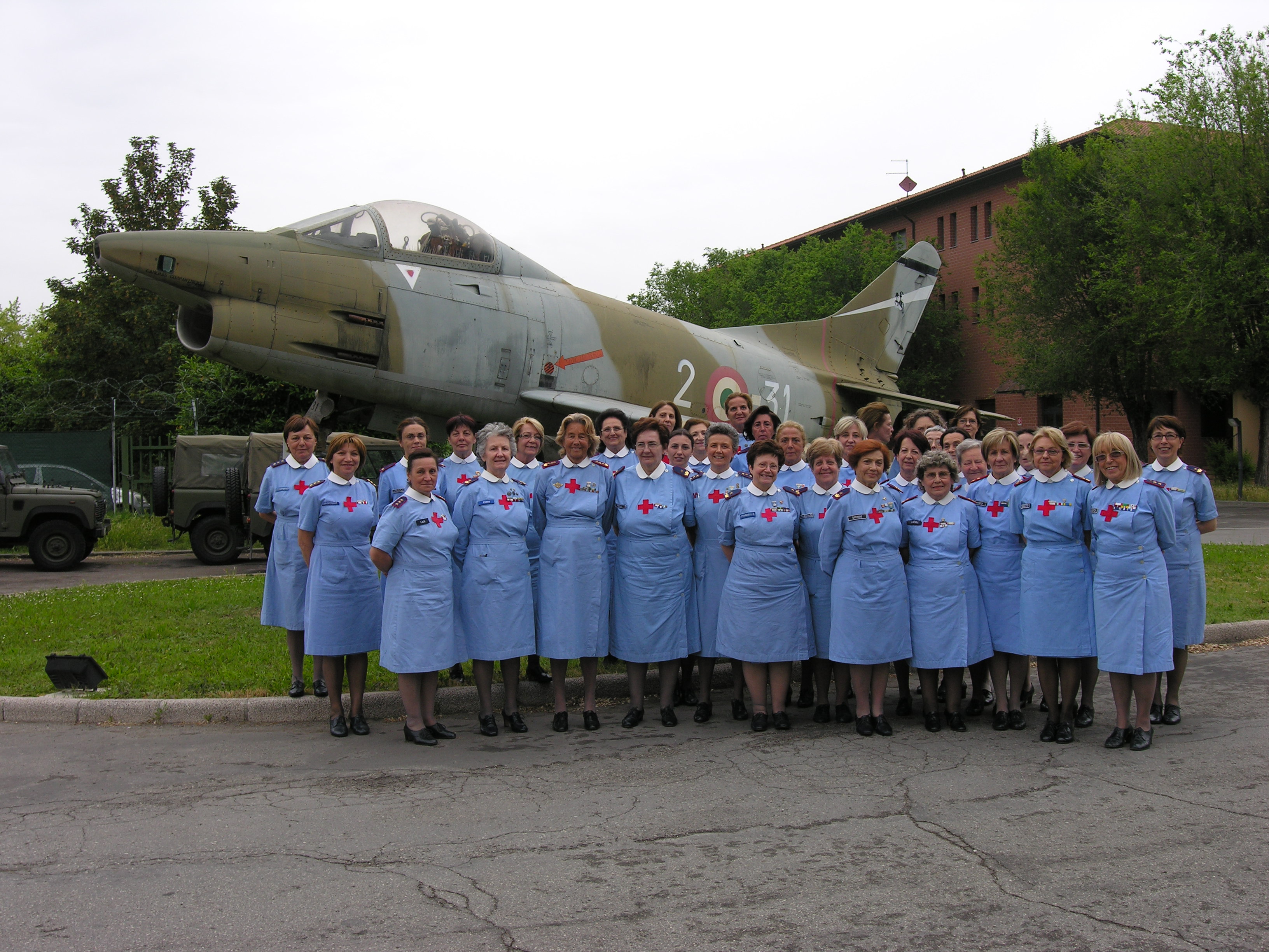 Foto di gruppo all'esterno con lo sfondo di un aereo militare
