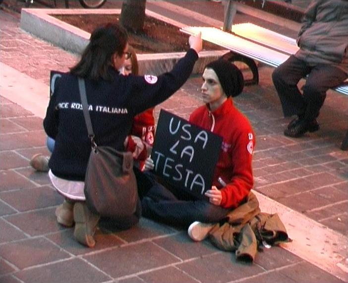 Volntaro seduto a terra con cartello "USA LA TESTA"