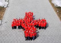 Immagine di persone disposte su una piazza che formano una croce rossa