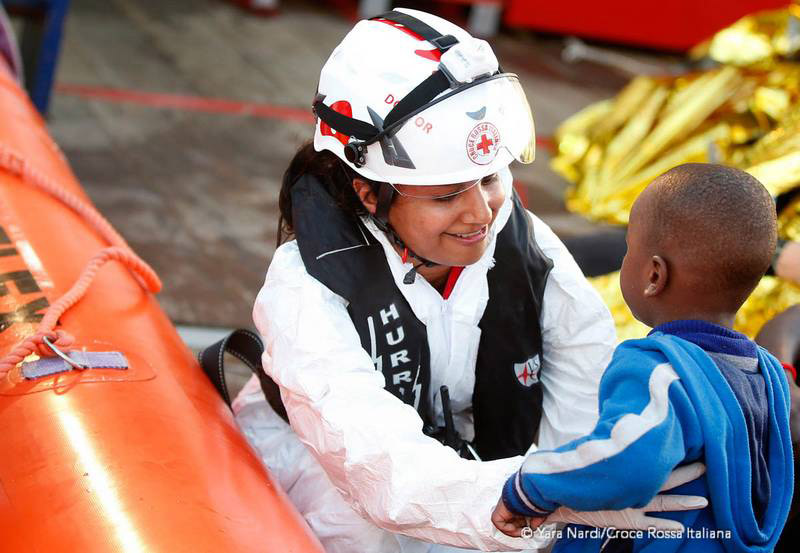 Un'operatrice Croce Rossa sorride a un bimbo appena salvato. Foto: Yara Nardi