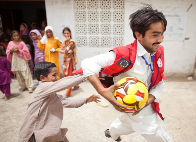 Un bimbo pakistano gioca  apalla con un volontario della Mezzaluna Rossa